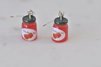 Close-up of strawberry jam jar earrings showing label detail and dark green lid
