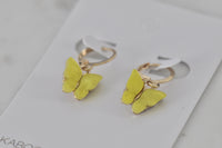 Close-up angled view of yellow butterfly charm earrings highlighting the gold huggie hoop and wing detail