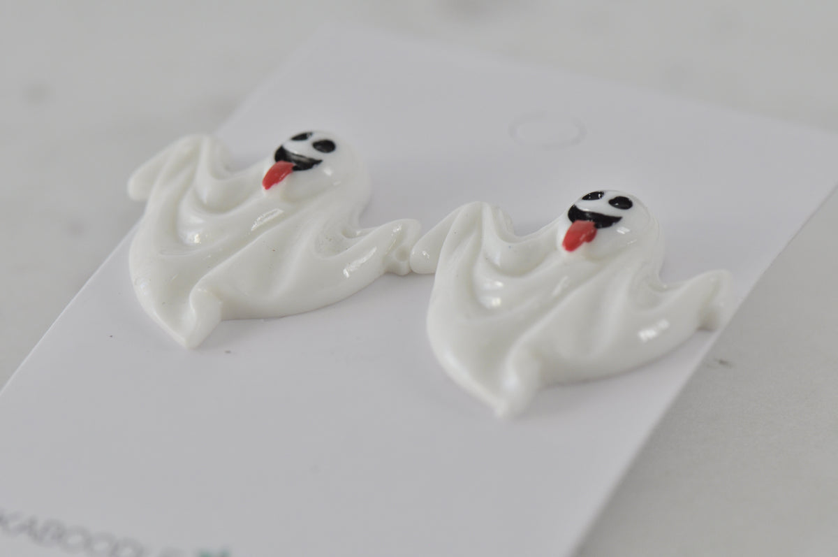 Close-up of two glossy white ghost stud earrings showing wavy shape and painted faces