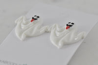 Close-up of two glossy white ghost stud earrings showing wavy shape and painted faces