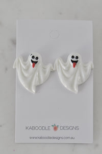 Pair of white ghost stud earrings with smiling tongue-out faces on a display card