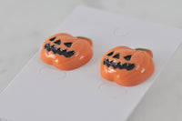 Close-up of two pumpkin stud earrings showing glossy resin finish and carved face detail