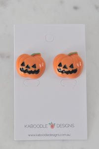Pair of orange resin jack-o-lantern stud earrings on a Kaboodle Designs card, front view