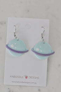 Pair of mint green Saturn planet earrings with lilac rings on Kaboodle Designs card