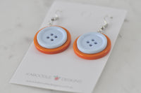 Pair of button earrings laid flat on branded card, top-down view