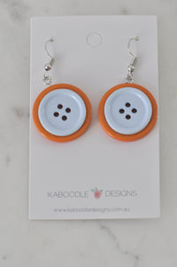 Orange and white plastic button drop earrings on Kaboodle Designs card