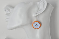 Single orange button earring worn on ear, close-up angle