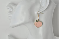 Peach-shaped enamel earring shown on ear for scale, gold hook and chain
