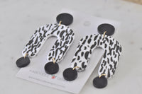 Overhead view of both black and white arch earrings laid flat showing print detail and gold jump rings