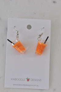 Pair of orange juice cup resin earrings with black straws on Kaboodle Designs card