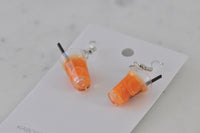 Overhead view of two orange juice drop earrings showing glossy resin and citrus swirl pattern