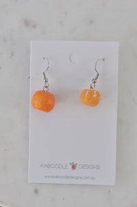 Two resin mandarin drop earrings in orange tones on a Kaboodle Designs card