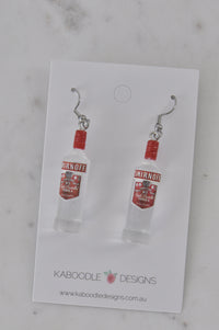 Close-up of vodka bottle earrings on card showing red label and cap detail