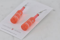 Angled close-up of the two bottle earrings on a Kaboodle Designs card showing label and hook detail