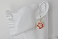Close-up of red enamel flower earring worn on ear, showing gold-tone outline and coloured centre