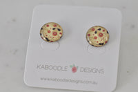 Round handmade stud earrings with cream background, red floral print and black leaf detail, shown on branded card