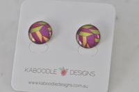 Round stud earrings with pink, purple, olive and mustard geometric pattern under glossy dome, on Kaboodle card