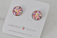 Round handmade stud earrings with pink, orange and mustard confetti dot pattern under glossy resin cover