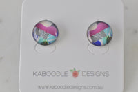 Pair of round stud earrings with abstract pink, teal and striped artwork on white display card