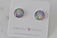 Round stud earrings with green, pink and purple abstract artwork under glossy resin, shown on card