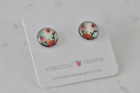 Pair of round stud earrings with hand-painted pink and red poppy artwork on mint background, displayed on card