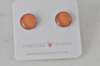 Round orange artwork stud earrings with glossy clear dome finish on Kaboodle Designs card