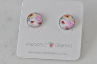 Round stud earrings with pink and yellow floral artwork under glossy clear cover, on Kaboodle card