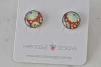 Round stud earrings with red, teal and gold mandala artwork on white Kaboodle card