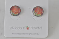 Pair of round handmade artwork stud earrings with orange, yellow and blue speckled pattern on card