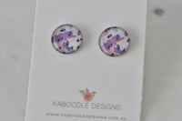 Round stud earrings on card with abstract purple, pink and navy speckled artwork under glossy dome