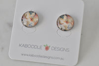 Round floral artwork stud earrings on a Kaboodle Designs card, close-up top view