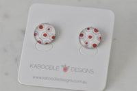 Round stud earrings with red dot and ring artwork design on white background, shown on card