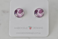 Pair of round flower artwork stud earrings in pink and purple on Kaboodle Designs card