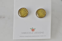 Round yellow stud earrings with black polkadot pattern and glossy finish, shown on card
