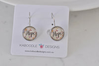 Round silver-tone Hope dangle earrings on Kaboodle Designs card, floral background under glass dome