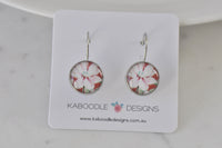Round silver-tone leverback earrings with pink and white floral design, front view on card
