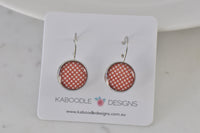 Round silver-tone dangle earrings with terracotta and cream polka dot pattern on display card