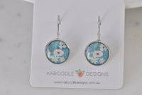 Round silver-tone leverback earrings with blue floral resin design, shown on jewellery card