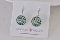Round leverback earrings with green and purple peacock feather print, on Kaboodle card