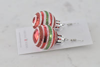 Close-up of two red glitter-striped bauble earrings resting on card