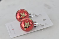 Red and gold Christmas bauble earrings resting on branded product card