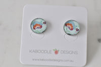 Round handmade stud earrings with mint green floral artwork and glossy resin dome, on Kaboodle card