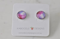 Round stud earrings on card with pink, purple and white watercolour-style artwork design
