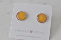 Pair of round golden yellow stud earrings with glossy domed finish on Kaboodle Designs card