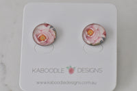 Pair of round stud earrings with pink rose artwork under glossy resin dome, shown on card