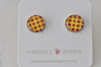 Pair of round stud earrings with red polka dots on yellow background, on Kaboodle Designs card