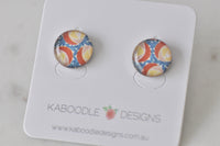 Round stud earrings on card with terracotta, mustard and blue geometric pattern under glossy resin
