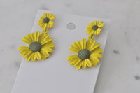 Close-up of yellow enamel daisy earrings showing textured green centres