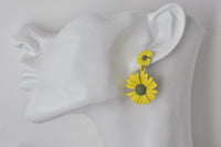 Yellow daisy dangle earring shown worn on ear for scale
