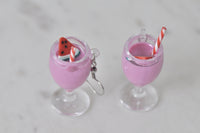 Close-up top view of two milkshake glass earrings with striped straws and a watermelon slice